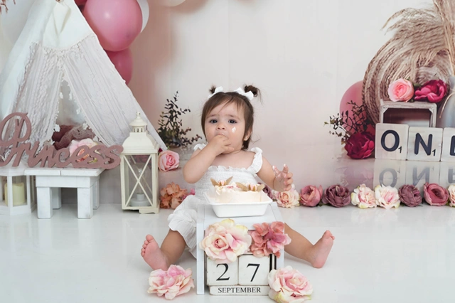 תינוקת יושבת בסטודיו בחגיגת smash cake בבגד לבן.