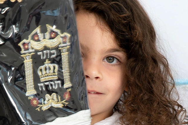 פניה של ילדה מחייכת מוסתרת חלקית על ידי כיסוי תורה רקום