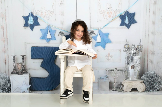 ילד יושב וקורא בספר, עם כיפה וחיוך, בסטודיו.