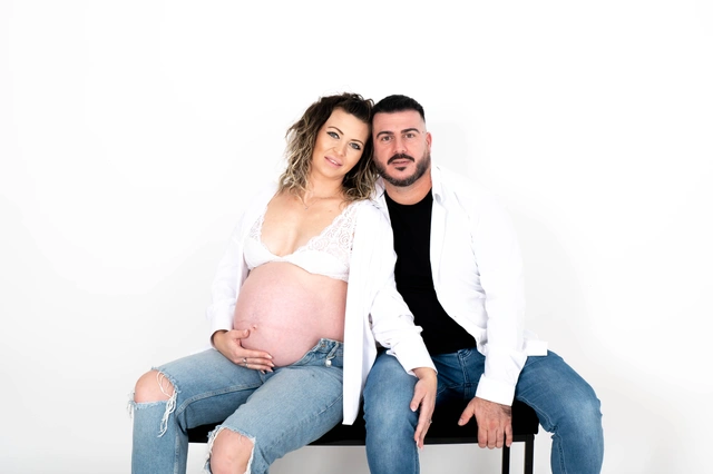 אישה הרה ובן זוגה יושבים ומביטים למצלמה