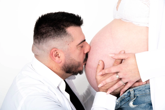 גבר חובק ומנשק בטן הריונית, עם ידיים מונחות עליה.