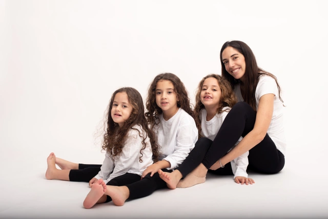 אמא ושלוש ילדות מחייכות ומחובקות על רקע לבן.