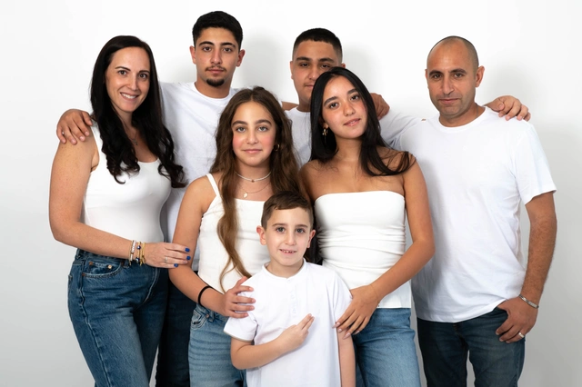 משפחה גדולה מצטלמת בחיוך בסטודיו לבן