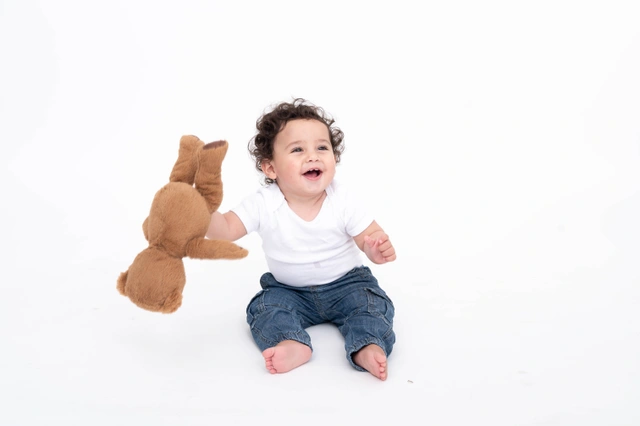 תינוק שמח יושב על רקע לבן ומחזיק בובת דוב.
