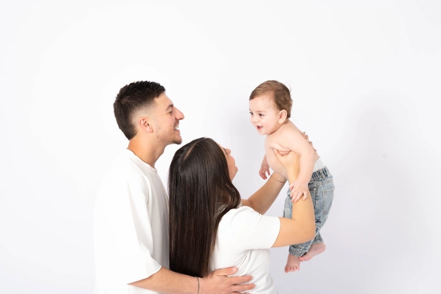 הורים מחייכים מרימים את תינוקם המאושר בסטודיו.
