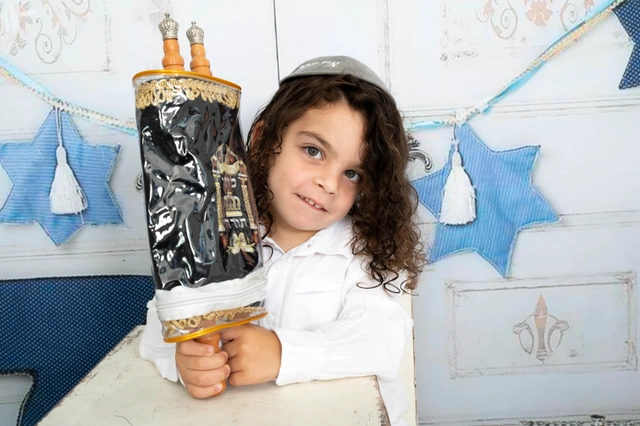 ילד אוחז בספר תורה מיניאטורי על רקע לבן דקורטיבי.