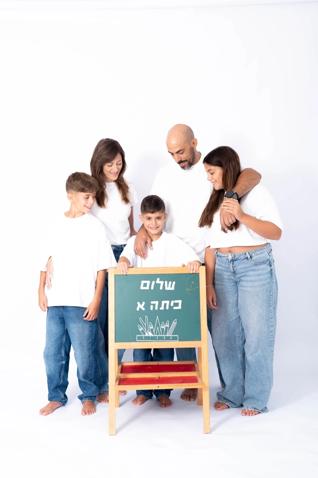 משפחה מול רקע לבן עם ילד המחזיק לוח עם כיתוב 'שלום כיתה א''