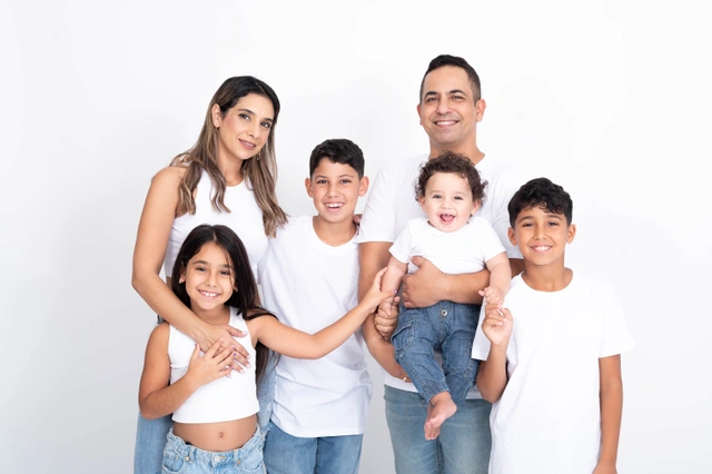 משפחה בת חמש נפשות מחייכת בסטודיו. הורים עם שלושה ילדים, כולל תינוק.