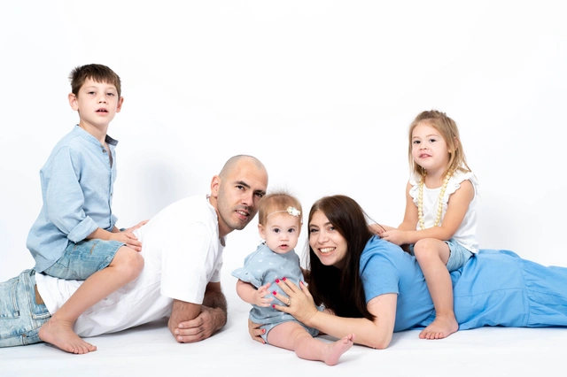 משפחה בת חמש נפשות מחייכת בצילום סטודיו. הורים שוכבים עם ילדיהם על גבם.