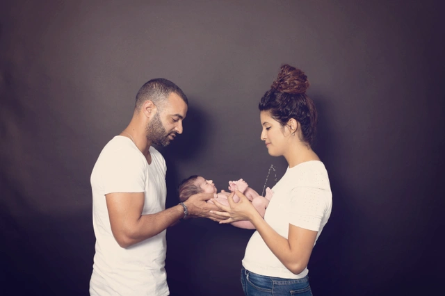 הורים מחזיקים בעדינות את תינוקם הניובורן יחד בצילום סטודיו.