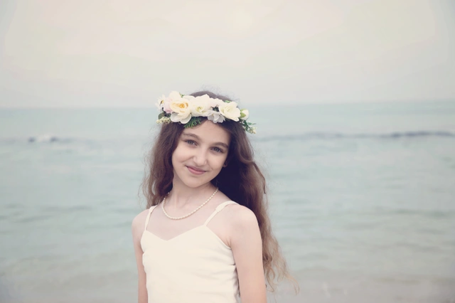 ילדה מחייכת למצלמה, לובשת זר פרחים, עם האוקיינוס ברקע.