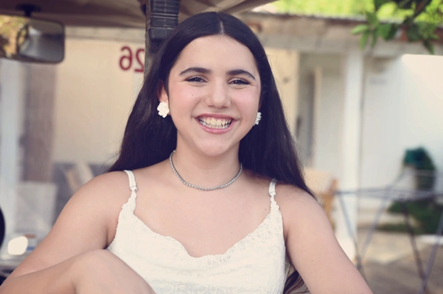 ילדה מחייכת לובשת שמלה לבנה ועגילי פרחים.