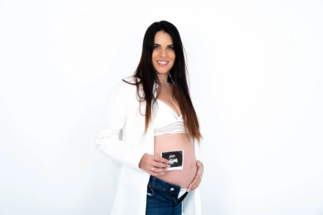 אישה הרה מחייכת ומחזיקה תמונת אולטרסאונד על בטנה החשופה.
